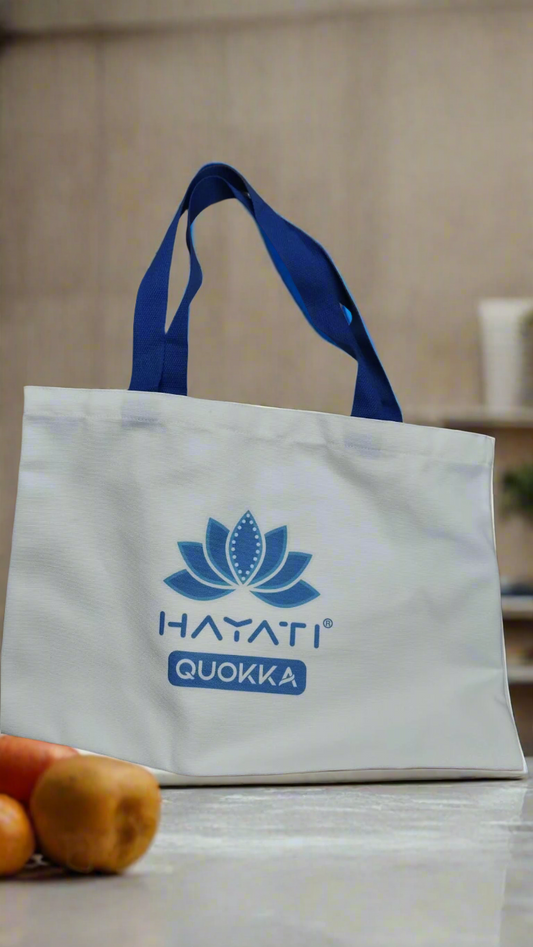 White tote bag with blue handles and 'HATATI QUOKKA' logo on a light background